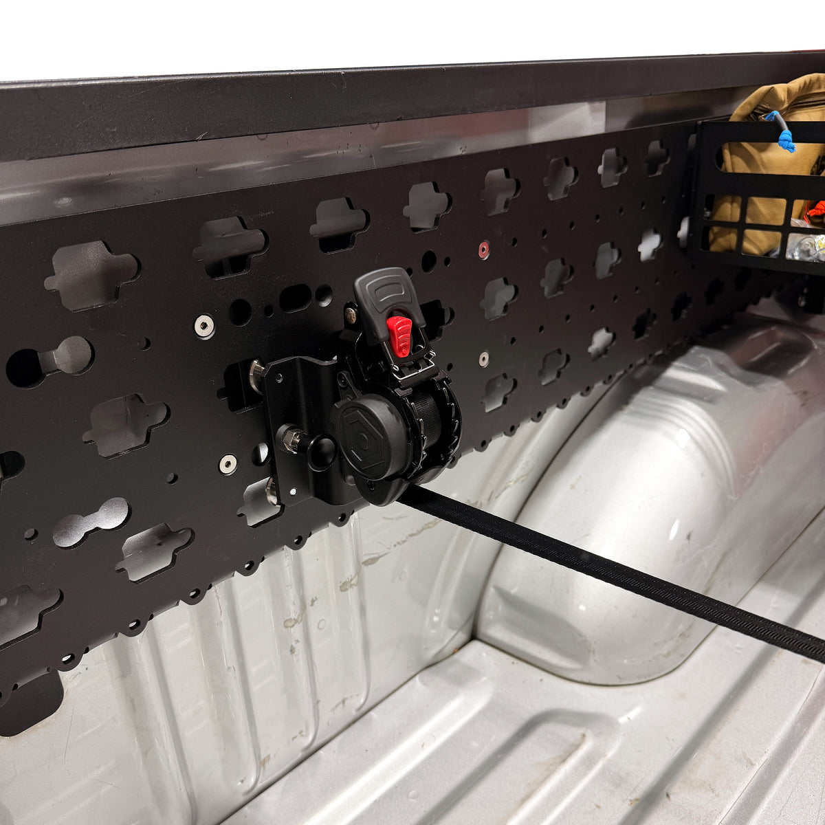 MOBUL Retractable Ratchet Strap Mount, strap extended, on a MOBUL panel in a truck bed.