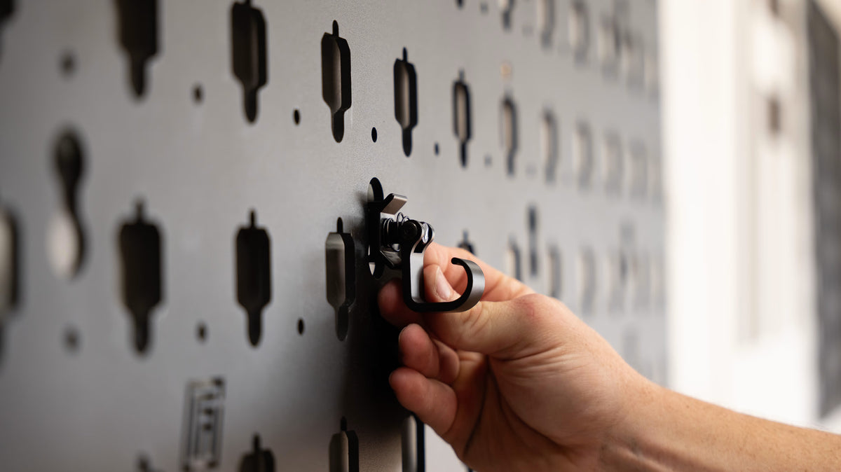 Closeup image of a hand securing an equipment hook to a metal MOBUL gear storage panel.